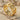 Close-up of the Cuban chain ring in gold vermeil resting on natural beach sand alongside small white seashells.