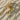 Premium gold vermeil rose flower pendant resting gracefully on textured desert sand beside a small rustic twig