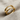 Side angle view of the abstract safety pin ring on woven cloth, emphasizing the elegant loop and smooth band craftsmanship.