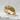 Close-up angled view of the feather diamond ring resting on a textured white surface highlighting the gold finish