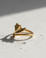 Gold vermeil dragon wing and arrow ring with textured details on white stone surface