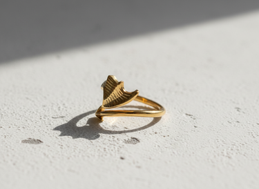 Gold vermeil dragon wing and arrow ring with textured details on white stone surface