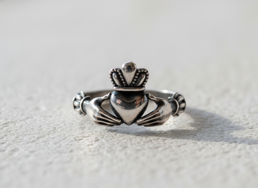 Straight angle shot of silver friendship ring with crowned heart and hands symbolizing love and loyalty