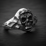 Close-up front view of silver hooded skull ring featuring oxidized eye sockets and textured hood on black slate
