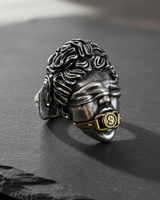 Silver Justice Ring with a brass dollar sign gag, shown at an angle on a dark slate surface to highlight the detail.