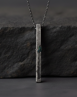 Front view of vertical silver bar necklace hanging against textured slate background