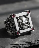 Front view of 925 sterling silver vampire skull ring with red gemstones on black slate background