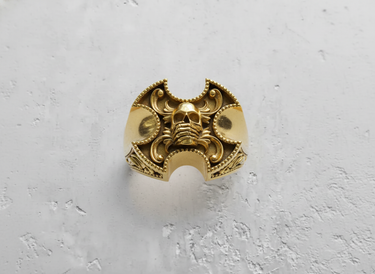 Front view of gold vermeil gothic skull ring with ornate filigree details on textured background