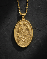 Gold vermeil oval medallion pendant featuring two skeletons kissing on a textured background on black stone