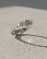 Angled view of 925 sterling silver Death Claddagh ring with skeletal hands holding a skull on stone background
