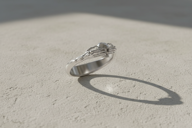 Angled view of 925 sterling silver Death Claddagh ring with skeletal hands holding a skull on stone background