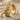 Close-up of handcrafted wood branch ring resting on textured sand highlighting the detailed gold vines and stones