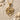Close-up of minimalist spider pendant crafted in 14K gold vermeil resting on sand next to seashells