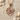 Close-up of minimalist spider pendant highlighting the smooth rose gold curves resting on white sand with seashells