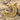 14K gold vermeil crescent star pendant resting on natural sand and pebbles highlighting its scrollwork.