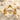 Close-up of gold vermeil chevron double ring resting on white sand surrounded by delicate sea shells.