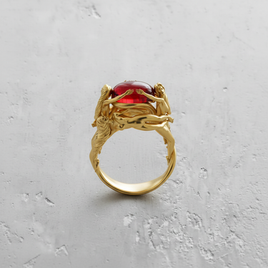 Gold vermeil Silver Three Graces Ring featuring sculpted female figures holding a red gemstone on texture