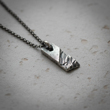 Angled view of 925 sterling silver bar pendant for men showing chiseled rock texture and dark oxidized finish