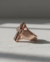 Side profile of rose gold plated silver Ankh ring with black stones on textured white background