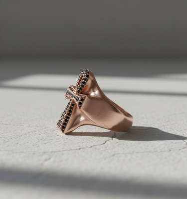 Side profile of rose gold plated silver Ankh ring with black stones on textured white background