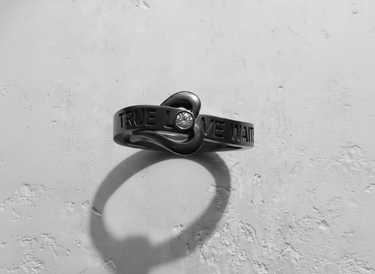 Black rhodium plated sterling silver true love waits ring with heart knot and crystal stone on textured background