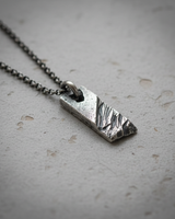 Angled view of 925 sterling silver rustic bar pendant on chain with distressed texture and oxidized finish