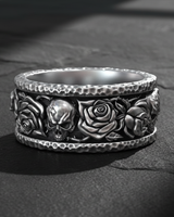 Close-up of handcrafted silver band ring showing detailed skull and rose relief pattern with oxidation