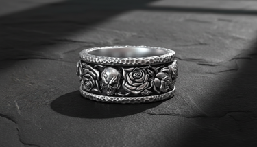 Close-up of handcrafted silver band ring showing detailed skull and rose relief pattern with oxidation