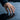 Lifestyle view of the oxidized silver double Venus pride ring worn on a woman's hand touching a dark water surface.