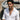 Man wearing oxidized silver rustic cross pendant over a white linen shirt standing outdoors next to a rustic wooden boat