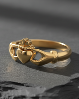 Gold vermeil Claddagh ring with hands holding heart and crown detail on textured grey surface