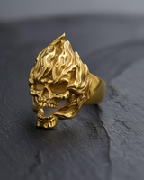 Front view of gold vermeil flaming skull ring featuring intricate fire details on textured black background