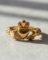 Front view of 14K gold vermeil Claddagh ring featuring hands holding a crowned heart on textured surface