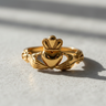 Front view of 14K gold vermeil Claddagh ring featuring hands holding a crowned heart on textured surface