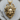 Close-up of the 14K gold vermeil Medusa head pendant resting on a natural wood slice highlighting detailed fangs
