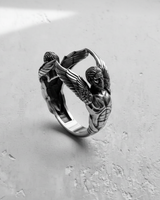 Angled view of handcrafted silver ring with winged guardians forming the band design